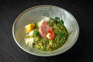 Risotto with spinach, avocado, salmon, shrimp and parmesan in a ceramic plate on a dark textured background. Restaurant menu Isolated on black