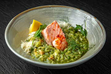 Risotto with spinach, avocado, salmon, shrimp and parmesan in a ceramic plate on a dark textured background. Restaurant menu Isolated on black