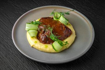 Airy mashed potatoes with liver in sauce in a ceramic plate on a dark textured background. Restaurant menu Isolated on black