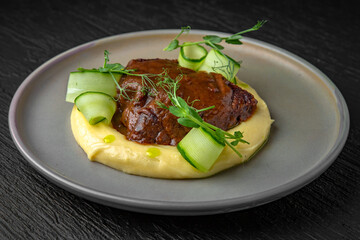 Airy mashed potatoes with liver in sauce in a ceramic plate on a dark textured background. Restaurant menu Isolated on black