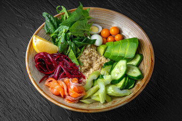 Buddha bowl with wholesome, nutritious and balanced ingredients. Salmon, beans, greens, vegetables in a ceramic plate on a dark textured background. Restaurant menu Isolated on black