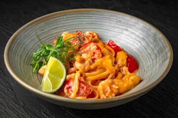 Delicious pasta with seafood and tomato sauce in a ceramic plate on a dark textured background. Restaurant menu Isolated on black