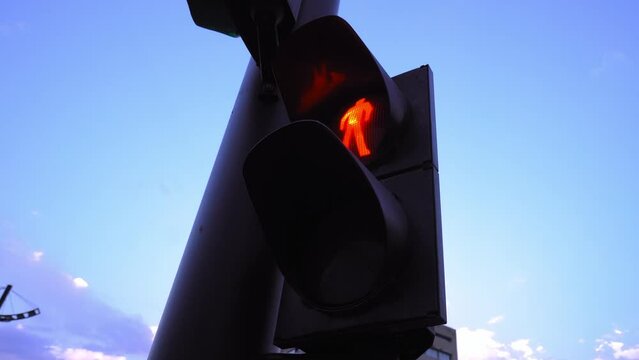Red traffic light with symbol of person standing against blue sky in city. Light sign to stop vehicle and lower speed limit so that they expect green resolution signal.