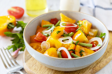 The concept of vegan or diet food. Tomato salad made from a mix of red and yellow tomatoes and green beans on a wooden table.