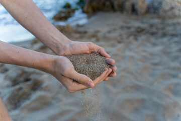 Hands of young man holding sand at beach