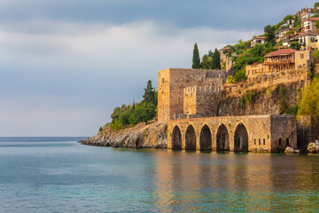 Fototapeta premium Ancient shipyard (Tersane) near of Kizil Kule tower in Alanya, Turkey (Turkiye) Famous tourist destination with high mountains. Part of medieval fortress (Alanya Castle) on the mountainside