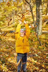 Happy adorable child girl laughing and playing yellow fallen leaves
