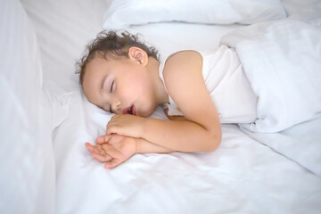 Sweet baby boy sleeps on white bed. Curly toddler sleeping alone