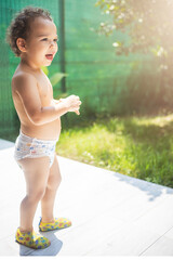 Happy curly toddler boy in a diaper playing in the backyard in the sun