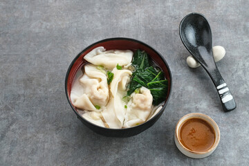 Yummy Wonton Soup (dumpling soup) or Pangsit Kuah served in bowl on dark background.

