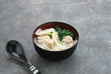 Yummy Wonton Soup (dumpling soup) or Pangsit Kuah served in bowl on dark background.
