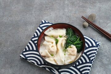 Yummy Wonton Soup (dumpling soup) or Pangsit Kuah served in bowl on dark background.
