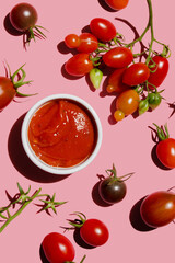 Tomato ketchup sauce and ripe red raw tomatoes on pink colored background, top view