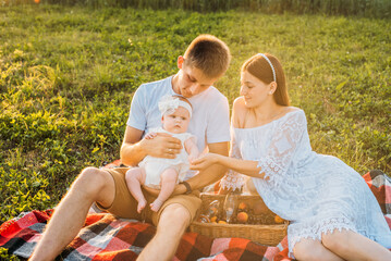 Young family of three - mother, father and daughter having picnic outdoors during beautiful sunset. Slow living and happy family concept