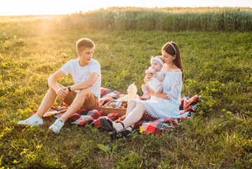 Young family of three - mother, father and daughter having picnic outdoors during beautiful sunset. Slow living and happy family concept