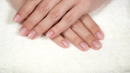 Pink natural nude look style womanly naildesign. Beautiful professional short naildesign on manicured healthy hands of european woman isolated on white towel background. Nails with pink gel polish