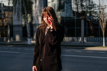 Fototapeta premium Young woman stanging on street having phone call looking away. Girl in coat talking on the phone outdoor