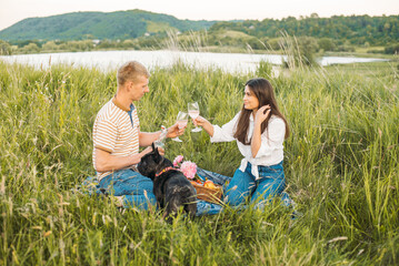 young happy couple having picnic with their french bulldog outdoors in the countryside during beautiful sunset. Romantic date near the lake