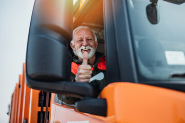 Senior garbage removal worker driving a waste truck. He is showing thumb up. - 524627720