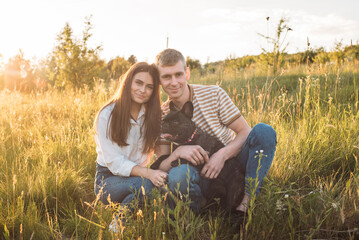 young happy couple having fun with their french bulldog outdoors in the countryside during beautiful sunset