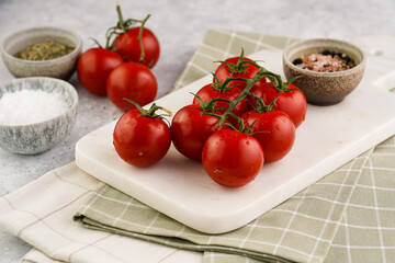 Fresh red tomatoes on branches on marble board on checkered kitchen towel, grey background