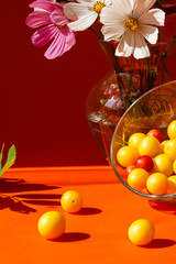Orange background. Glass bowl with fruit. Yellow plums on an orange background. Bright light and shadow. Art minimal composition, autumn still life.