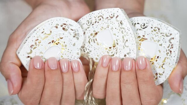Woman holding white metal garland string with lights and white hearts. Nails manicured in pastel pink natural color. 4k stock video of two female hands after beauty spa salon procedures