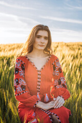 young beautiful woman wearing ukrainian traditional embroidered dress in wheat field during sunset. Stand with Ukraine