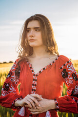 close up shot of young beautiful woman wearing ukrainian traditional embroidered dress in wheat field during sunset. Stand with Ukraine