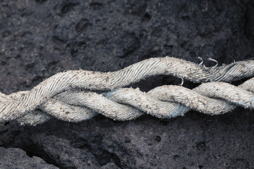 Three strands unravelled old white rope on black rock