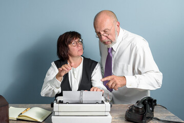 In the office. Retro style. Eldery boss dictating text to his secretary. Woman works on the old...