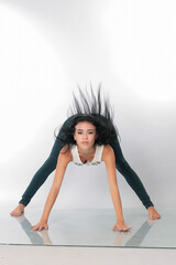 a pretty girl brunette stretching instructor, yoga, trainer, danser, posing in the studio on a white background in lasins and T-shirt