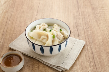 Yummy Wonton Soup (dumpling soup) or Pangsit Kuah served in bowl on wooden background.
