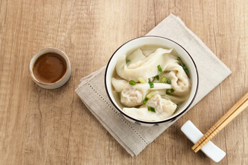 Yummy Wonton Soup (dumpling soup) or Pangsit Kuah served in bowl on wooden background.
