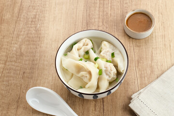 Yummy Wonton Soup (dumpling soup) or Pangsit Kuah served in bowl on wooden background.
