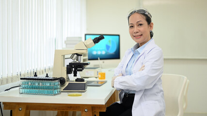 Shot of middle aged scientist sitting in front of microscope at research laboratory and smiling to camera