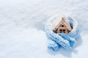 Cozy warm house concept. Christmas and New Year background. Christmas toy house wrapped in a warm blue scarf in the snow.