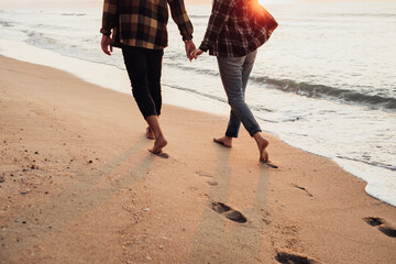 Unrecognisable couple meeting sunrise on the seashore, man and woman holding by hands walking along the coastline