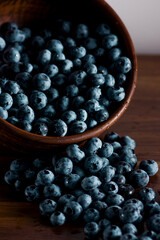 A handful of fresh blueberries in a clay deep plate with patterns on a wooden kitchen table in a dark modern interior. Topics of food, products, vitamins, health, cooking.
