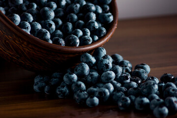 A handful of fresh blueberries in a clay deep plate with patterns on a wooden kitchen table in a dark modern interior. Topics of food, products, vitamins, health, cooking.