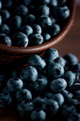 A handful of fresh blueberries in a clay deep plate with patterns on a wooden kitchen table in a dark modern interior. Topics of food, products, vitamins, health, cooking.