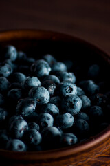 A handful of fresh blueberries in a clay deep plate with patterns on a wooden kitchen table in a dark modern interior. Topics of food, products, vitamins, health, cooking.