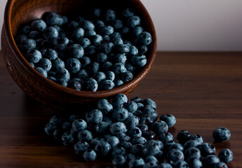 A handful of fresh blueberries in a clay deep plate with patterns on a wooden kitchen table in a dark modern interior. Topics of food, products, vitamins, health, cooking.
