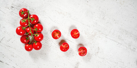 Vibrant small red tomatoes with green vines on white stone like board, view from above, empty space for text right side