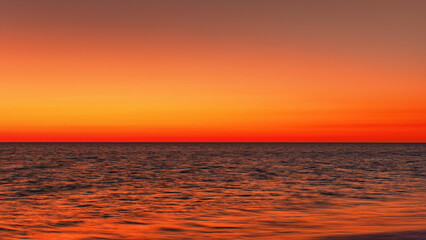 Vibrant orange red sky reflecting in calm ocean after sunset. Minimal landscape photo with space...