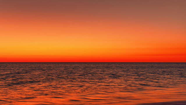 Vibrant orange red sky reflecting in calm ocean after sunset. Minimal landscape photo with space for text