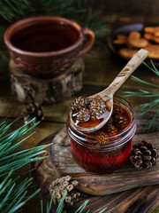 Honey from young pine cones. Wooden teaspoon with pine cones inside. Jam in a glass jar, standing...