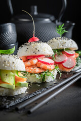 Unique sushi burger with vegetables and seafood on strone plate.