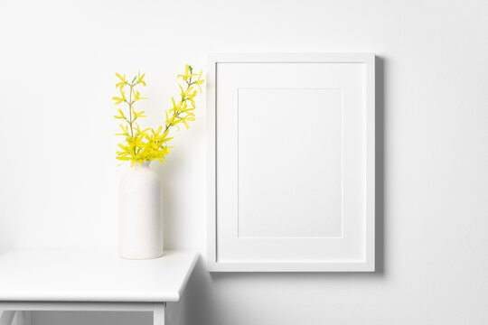 Portrait picture frame mockup on white wall with spring yellow flowers twig