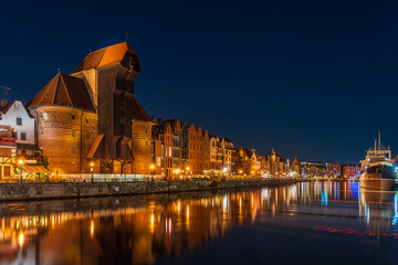 Naklejka premium Night illumination of the embankment of the old town in Gdansk, Crane on Motława, reflections of lanterns of the embankment in the river Motława, Poland tourist attractions